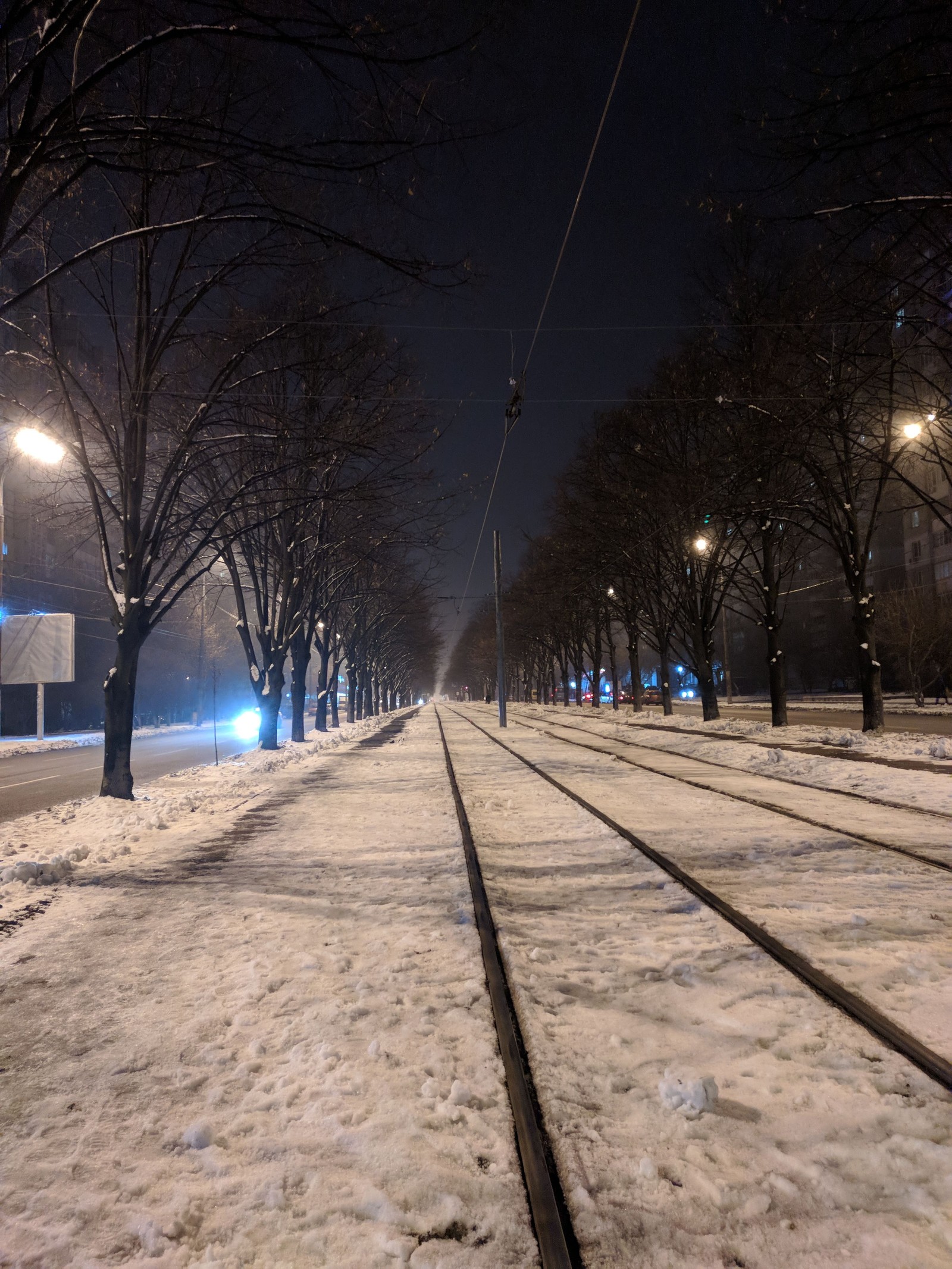 Uma rua nevada com uma linha de trem e postes de luz (ferrovia, caminho, vida, noite)