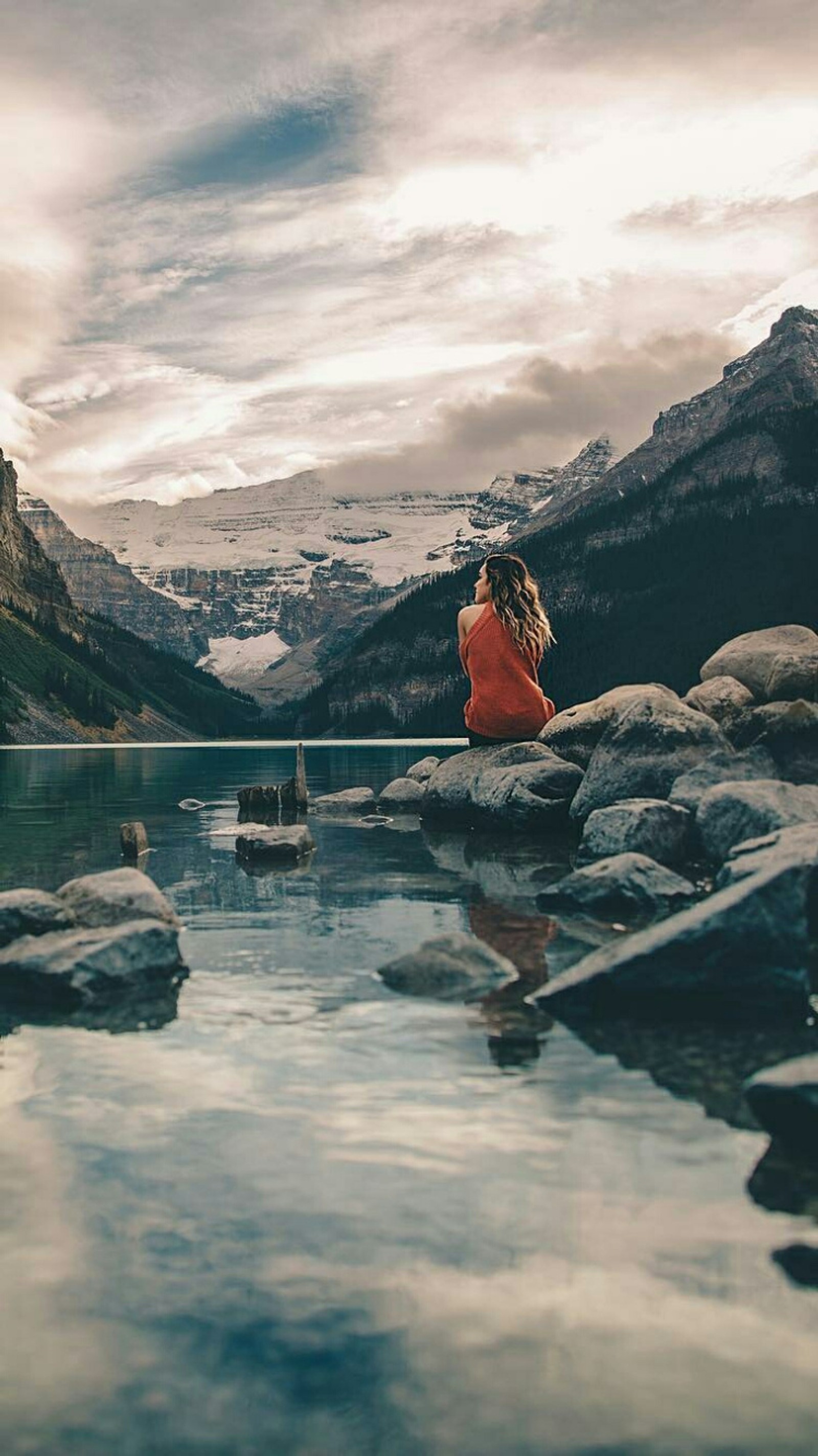 Eine frau sitzt auf einem stein am wasser (allein, neben, mädchen, see, stimmung)