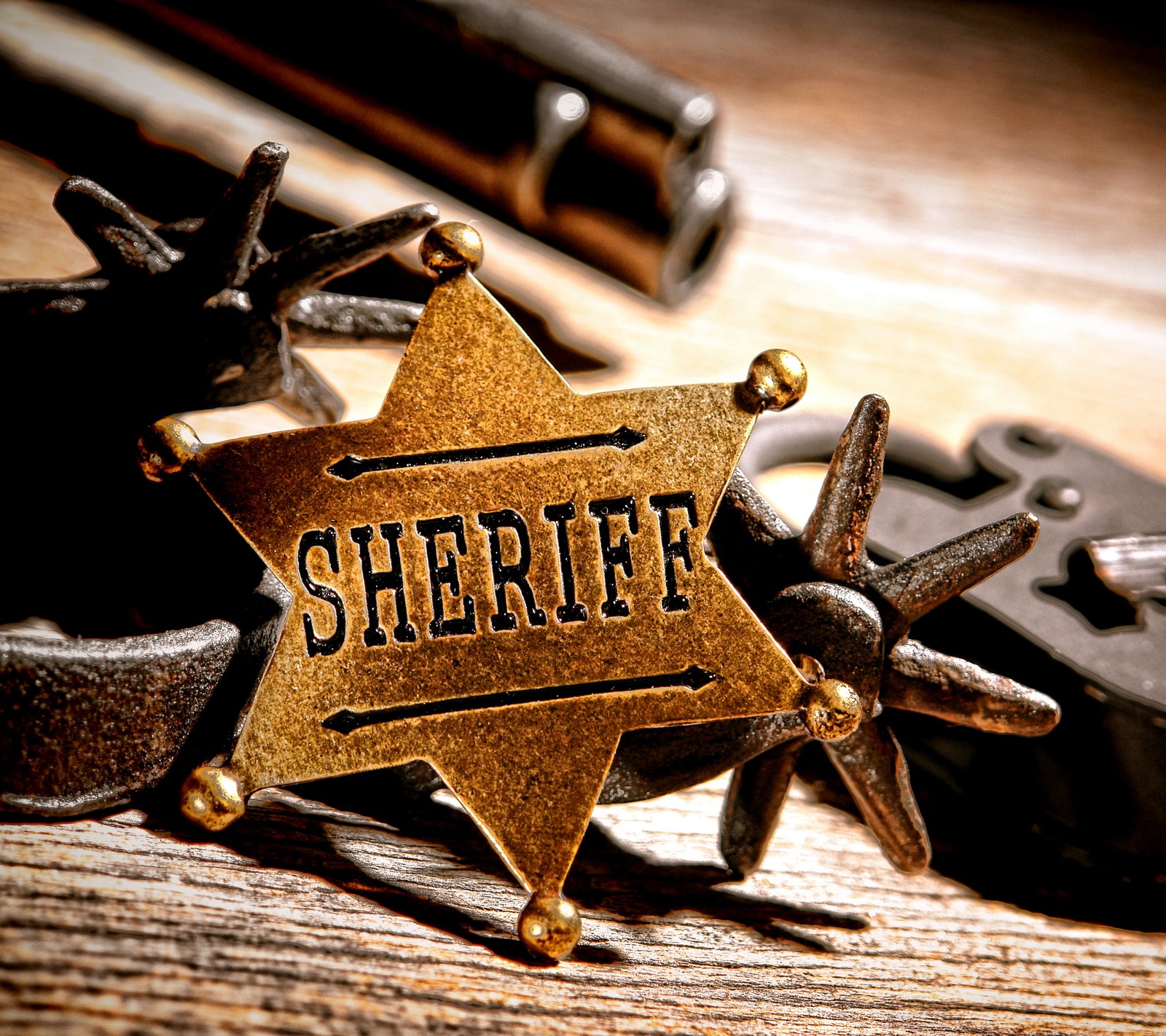 Auf einem holztisch liegt ein sheriff-abzeichen mit einer waffe (amerikanisch, abzeichen, gold, golden, pistole)