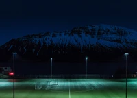 Terrain de football illuminé sous un ciel crépusculaire avec des montagnes enneigées