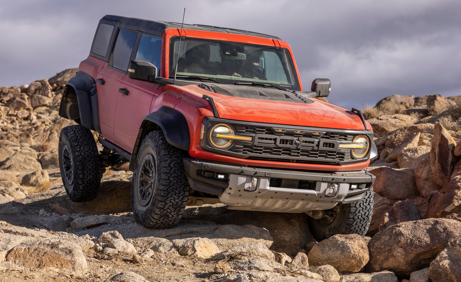 Um jeep vermelho dirigindo em terreno rochoso com céu nublado (ford bronco raptor, suv off road, off road, 2022, 5k)