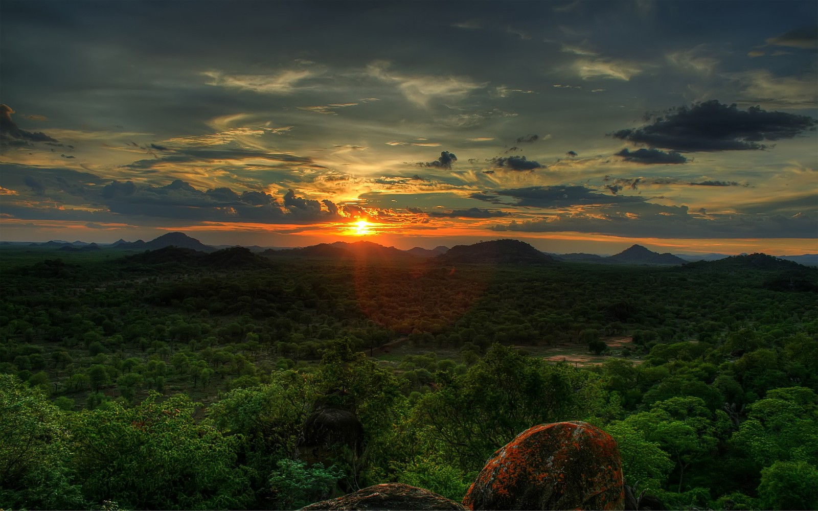 A view of a sunset over a green forest and mountains (nature, sunrise, vegetation, morning, sunset)