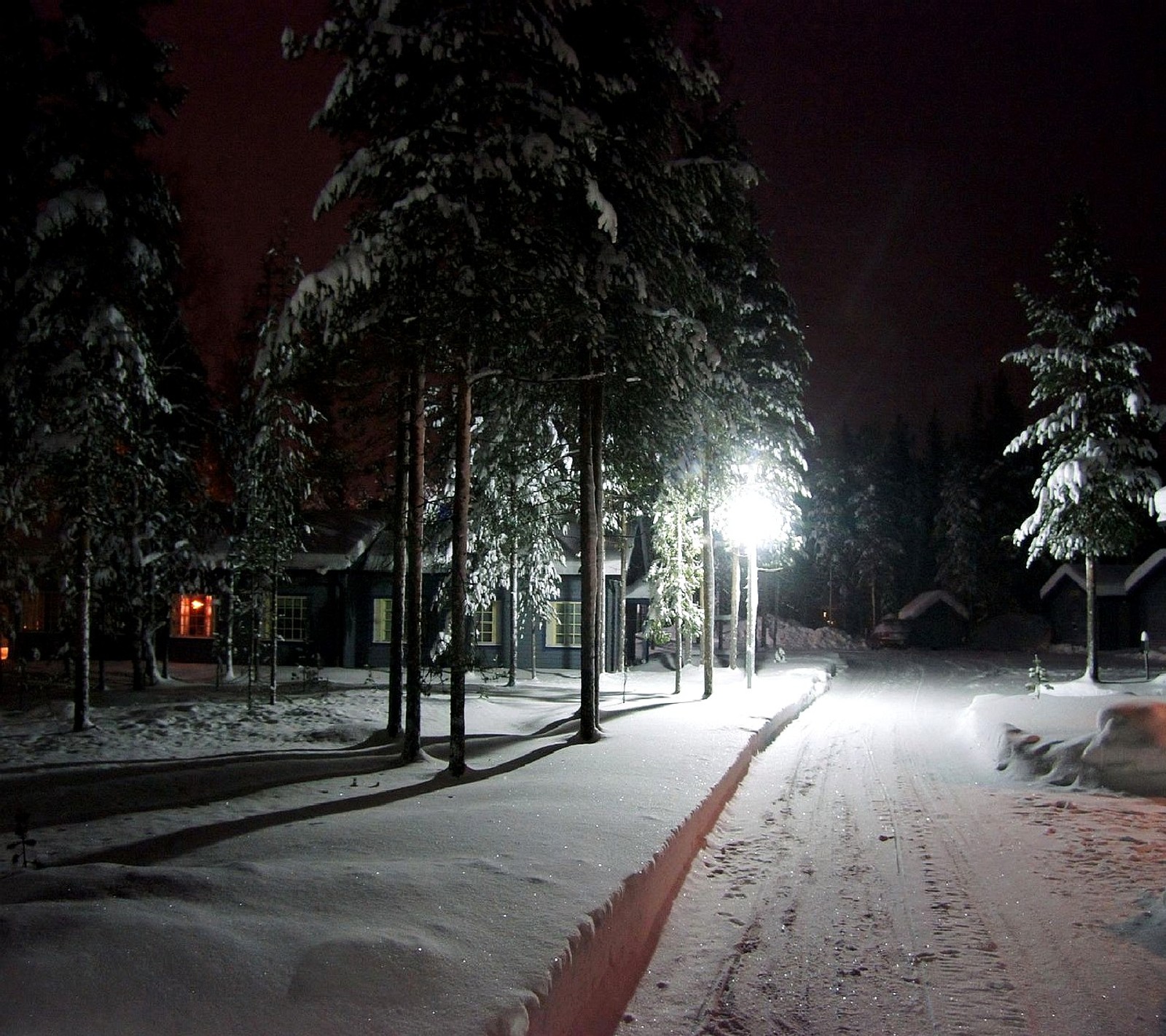 Une route enneigée avec un lampadaire et des arbres en arrière-plan (hiver)