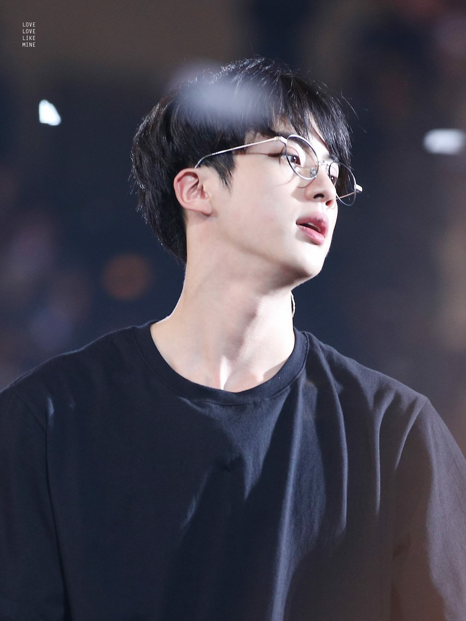 Un homme déformé avec des lunettes et une chemise noire qui regarde vers le haut (bts, jin, scène)