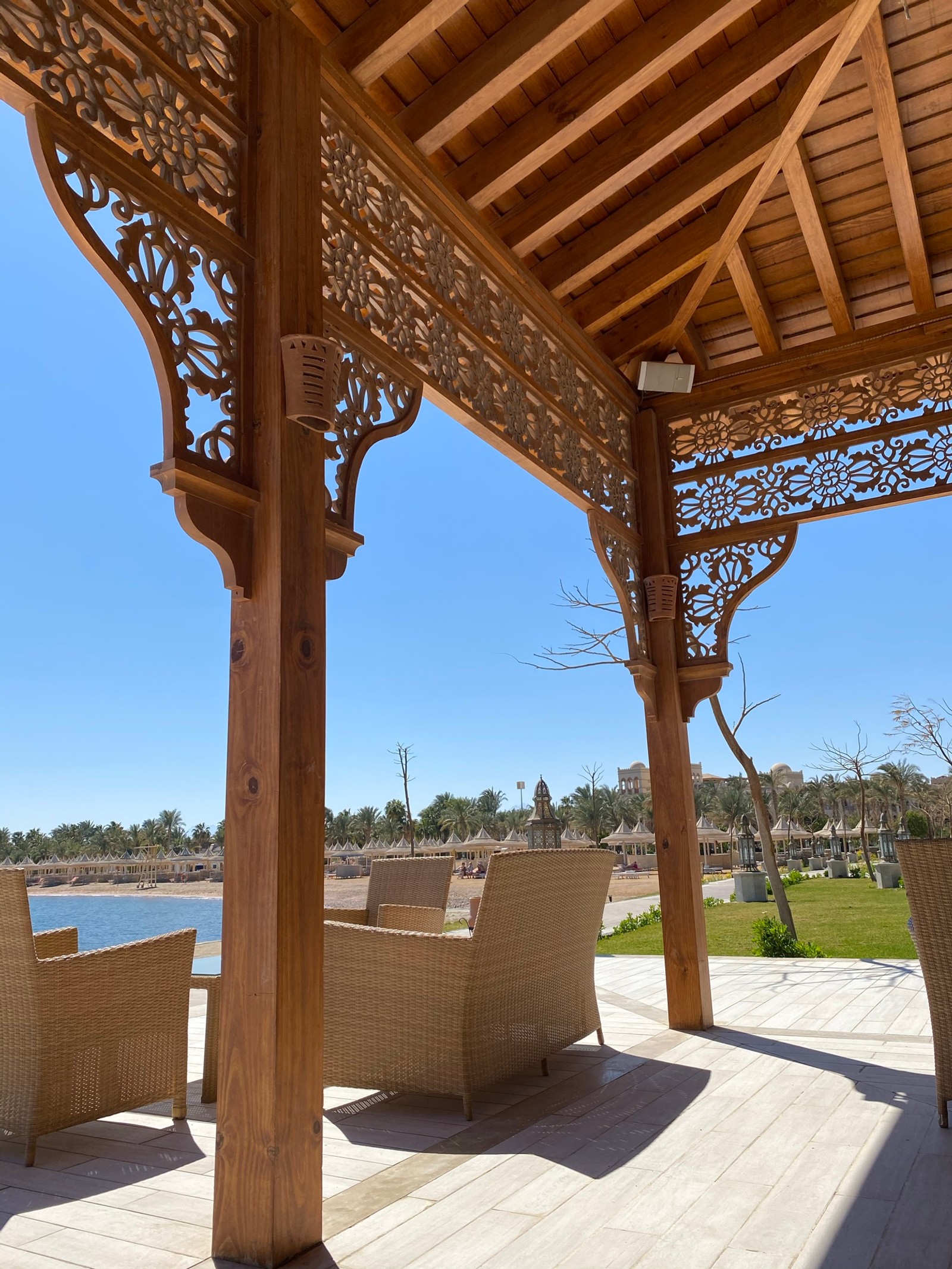 Há um gazebo de madeira com cadeiras de vime e uma mesa (sombra, madeira, planta, arquitetura, iluminação)