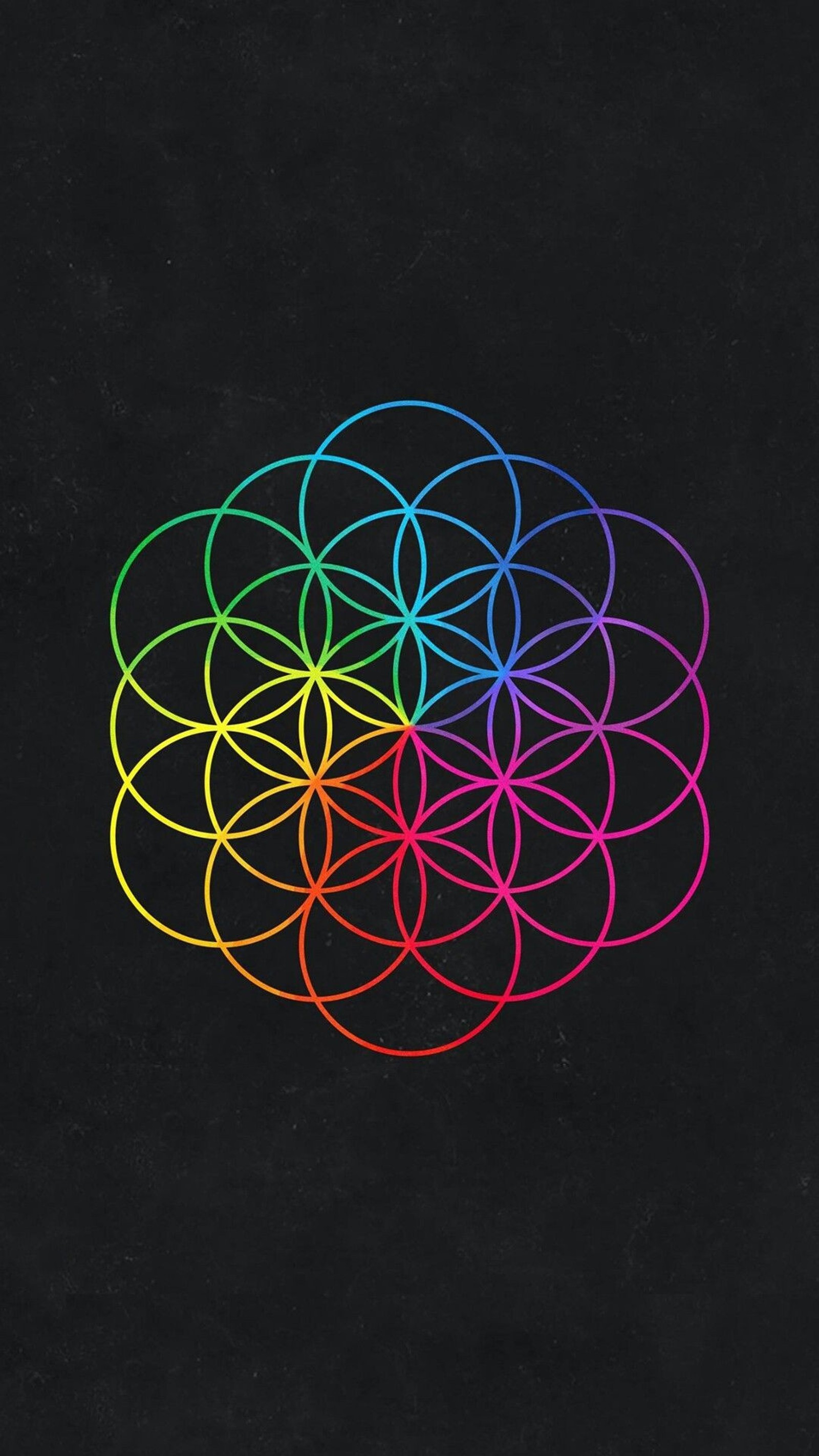 Un primer plano de un fondo negro con una flor de la vida de colores del arcoíris (coldplay, magia, música)