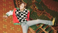 Onew se détend parmi des chaises empilées dans une tenue à carreaux élégante