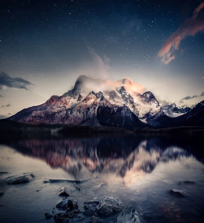 Des montagnes majestueuses se reflètent dans un lac tranquille sous un ciel étoilé au crépuscule, enveloppées de brouillard et des teintes sereines du coucher de soleil.