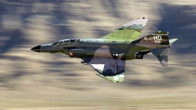 McDonnell Douglas F-4 Phantom II в полете, демонстрируя свой элегантный дизайн и военную камуфляжную окраску на фоне rugged.