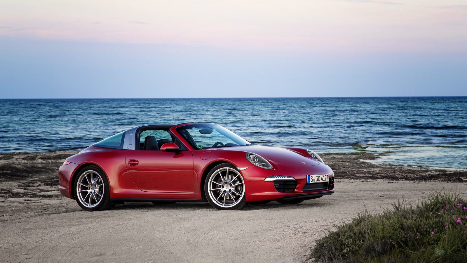 Un coche deportivo porsche rojo estacionado en una playa cerca del océano (coche, porsche, convertible, supercoche, coche deportivo)