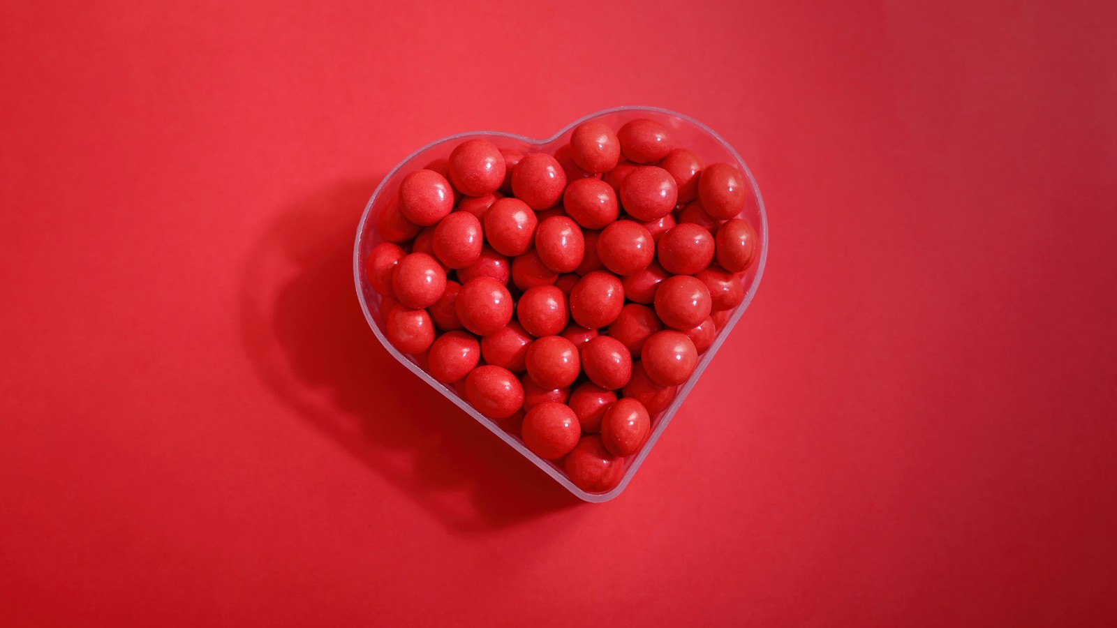 Un gros plan d'un récipient en forme de cœur rempli de bonbons rouges (forme de cœur, bonbons au sucre, fond rouge, 5k, cœur damour)