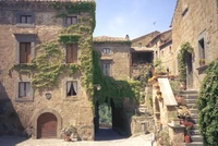 Encantadora viela medieval em uma pitoresca vila romana, exibindo edifícios de pedra adornados com vegetação exuberante e flores vibrantes.