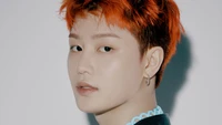 Taeil from NCT 127 showcasing a striking profile with vibrant orange hair and a stylish outfit.