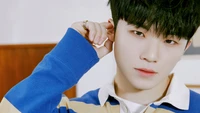 Woozi from Seventeen in a stylish striped sweater, playfully touching his ear with a captivating gaze.