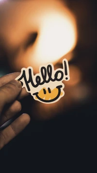 Nahaufnahme einer Hand, die einen 'Hallo!' Smiley-Aufkleber hält