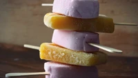 Colorful frozen desserts stacked on wooden sticks, showcasing sweet strawberry and fruity flavors.