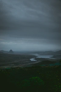 Nebeliger Hochlandlandschaft mit See und Bergen unter einem bewölkten Himmel