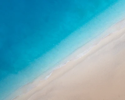 Aerial view of a tranquil beach with soft, sandy shores meeting the vibrant blue ocean.