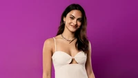 Camila Mendes in einem stilvollen weißen Kleid vor einem lebhaften lila Hintergrund.