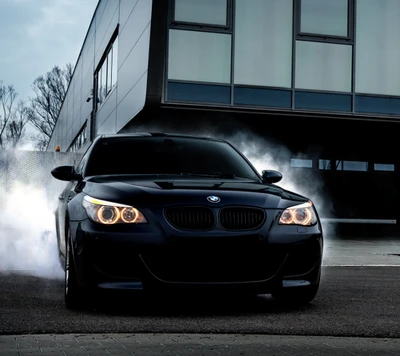 BMW M5 preto em movimento, emitindo fumaça contra um fundo de edifício moderno.