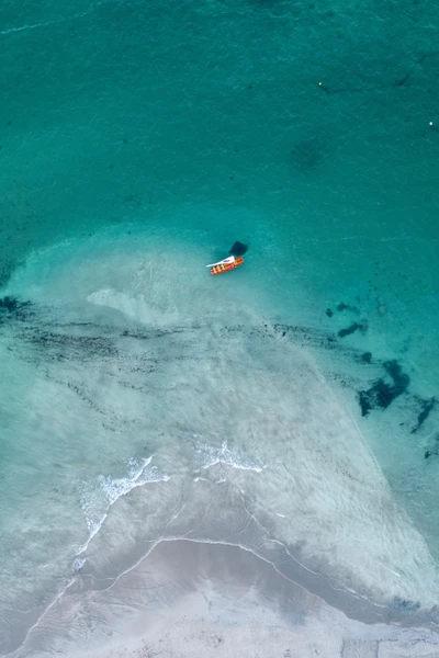 Eaux turquoise vibrantes et un bateau solitaire sur une plage tropicale sereine.