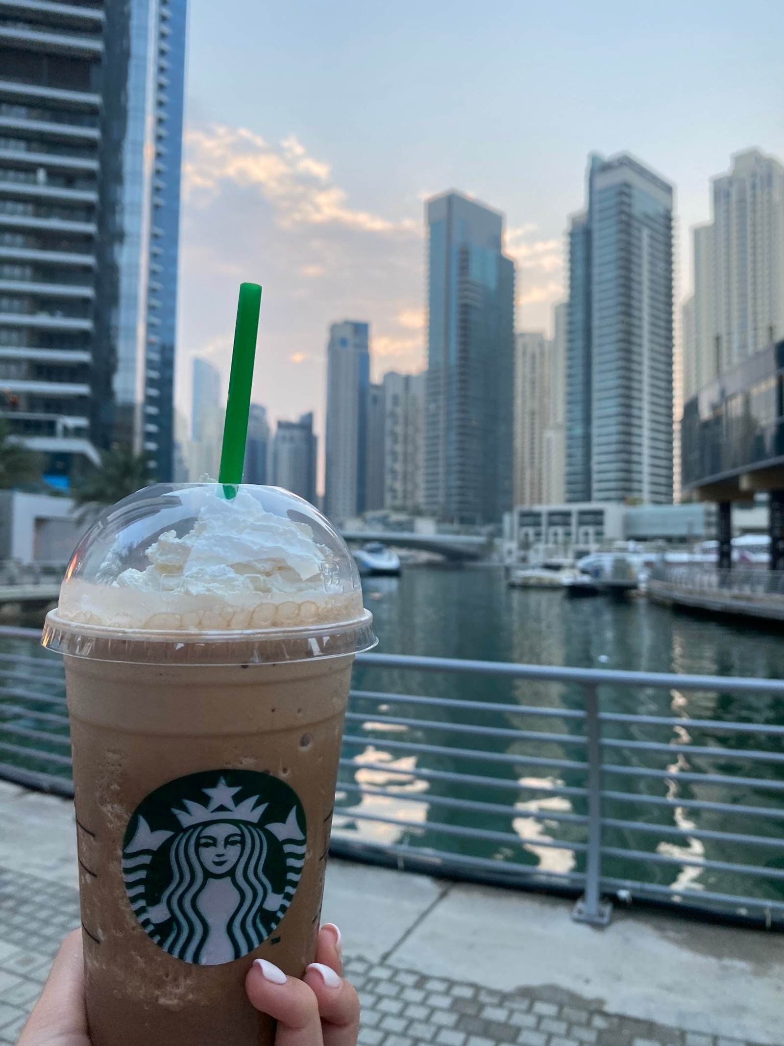 Ледяной кофе starbucks в пластиковом стакане с трубочкой на фоне городского горизонта (дубай, dubai, вода, башенный блок, напиток)