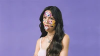 Olivia Rodrigo with colorful face stickers and playful expression against a purple backdrop.