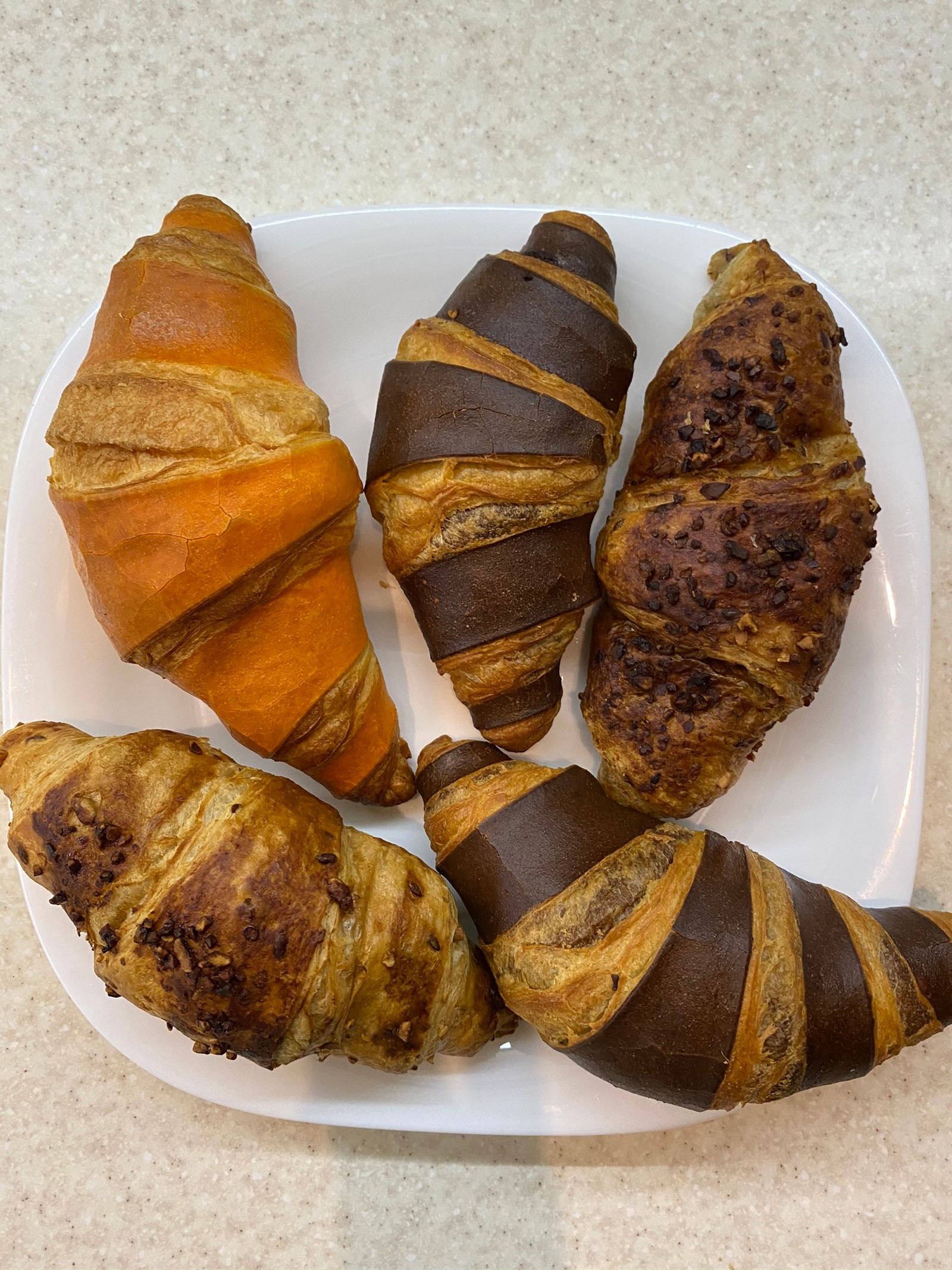 Hay cuatro croissants en un plato sobre una mesa (material natural, comida reconfortante, comida chatarra, productos horneados, comida rápida)