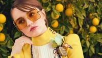 Kaitlyn Dever en un vibrante atuendo amarillo con gafas de sol de gran tamaño, rodeada de limoneros.