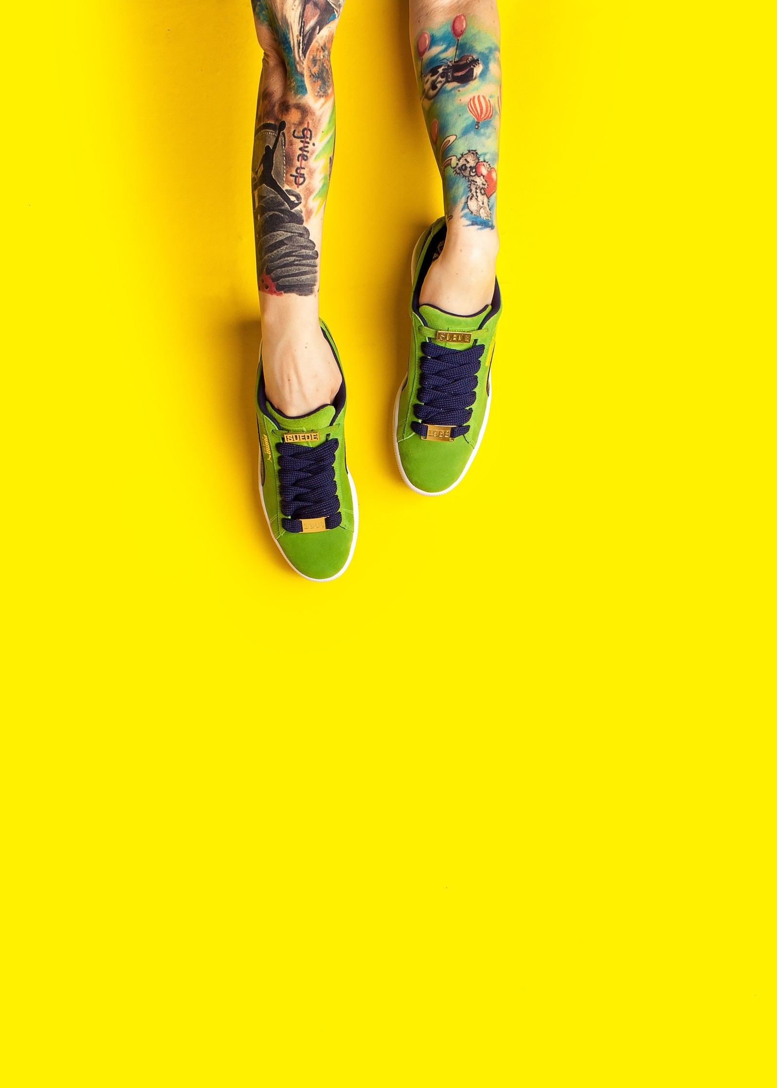 Someone with tattoos on their legs and green shoes on a yellow background (shoe, sneakers, footwear, green, yellow)