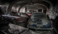 Coches vintage abandonados en un garaje polvoriento con paredes de ladrillo, que muestran la historia automotriz clásica.