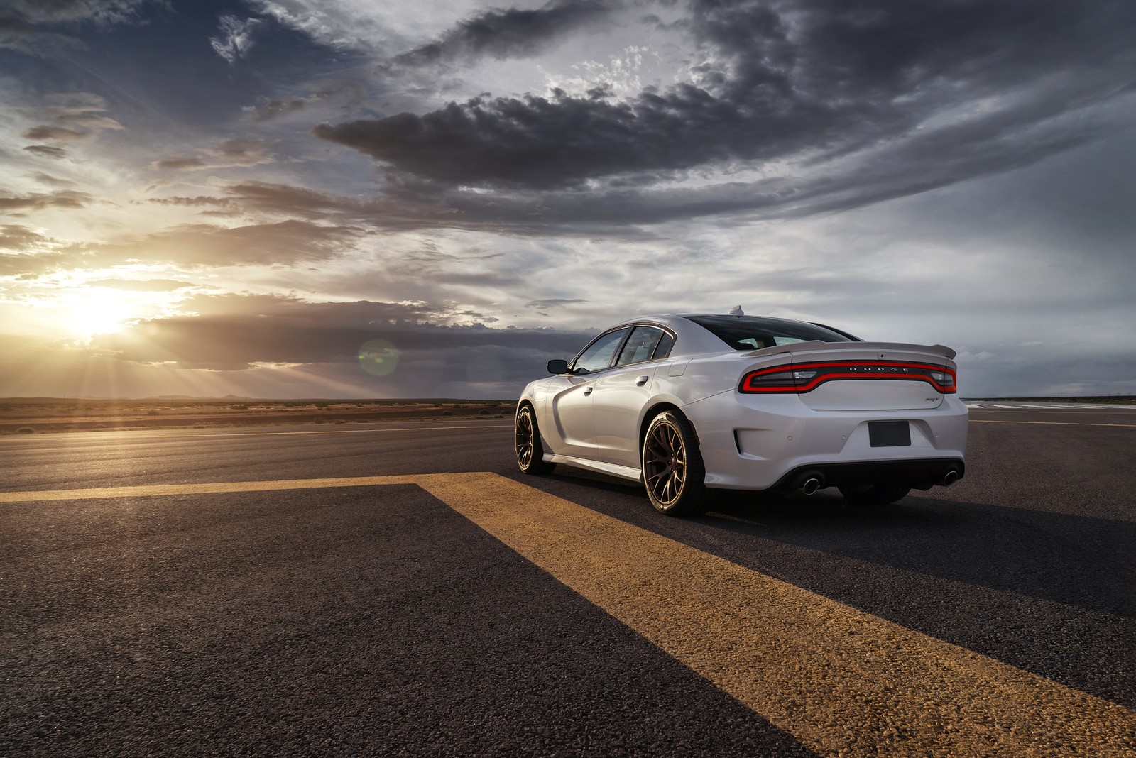 Une voiture blanche roulant sur une route avec le soleil se couchant en arrière-plan (dodge, voiture, supersportive, voiture de sport, hellcat)