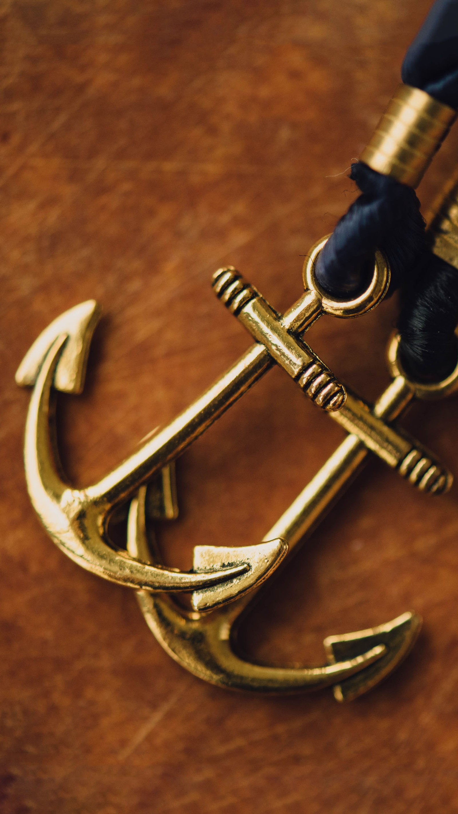 There is a gold anchor and a black cord on a table (anchor, love)