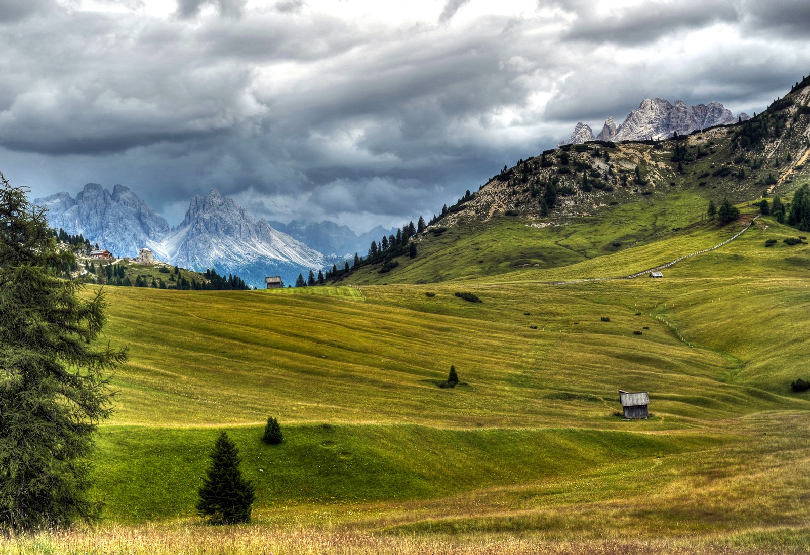 Arafed view of a green field with a small house in the distance (grassland, alps, italy, mountain, mountain range)