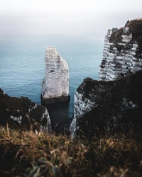 Majestic cliff rising from the tranquil blue sea, flanked by rocky shores under an expansive sky.