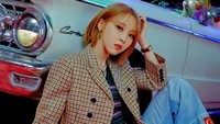 Moonbyul de Mamamoo irradia confianza con un atuendo elegante, sentada contra un fondo de coche vintage.