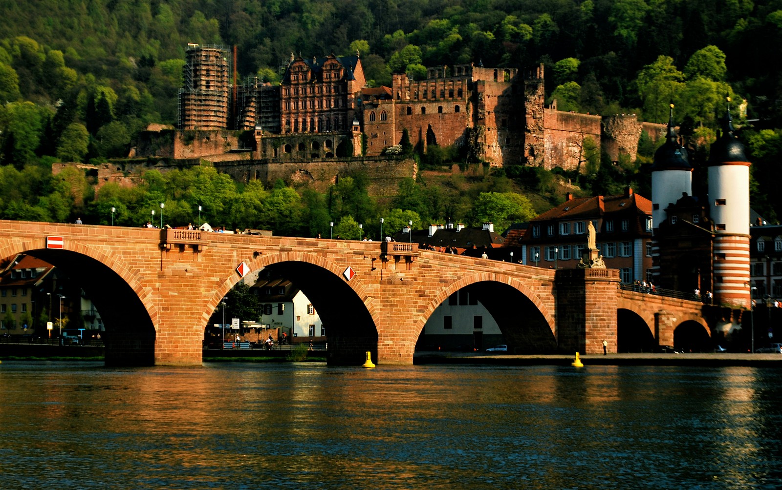 Eine brücke über einen fluss mit einem schloss im hintergrund (heidelberg, bogenbrücke, brücke, fluss, wasserstraße)