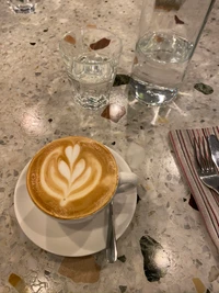 Cappuccino elegante con intrincado arte latte servido en una mesa texturizada junto a un vaso de agua.