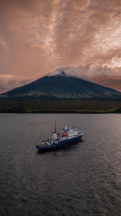 Una serena embarcación navega por un lago tranquilo con una majestuosa montaña cubierta de nubes al fondo.