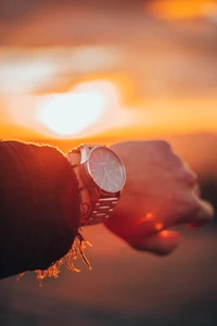 Time at Sunset: A Hand Reaches for the Watch Amidst an Orange Sky