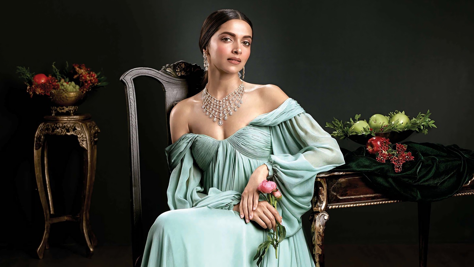 Uma mulher em um vestido verde sentada em uma cadeira com uma rosa (deepika padukone, celebridade, atriz, bollywood, morena)