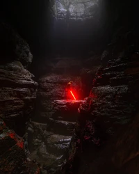 Caverna oscura con una figura empuñando un sable de luz rojo entre rocas similares a lava