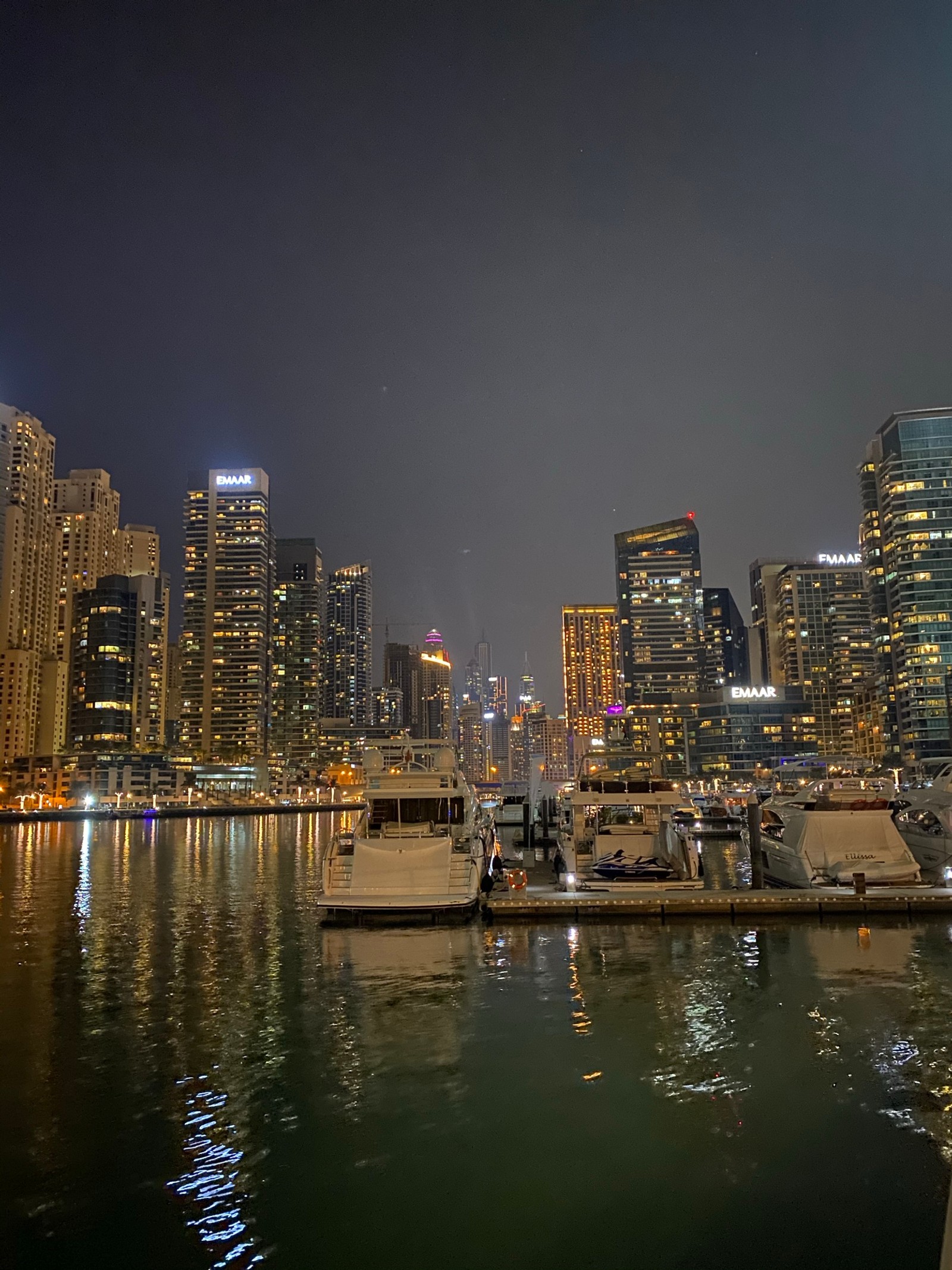 Barcos estão ancorados na água em frente a uma cidade à noite. (dubai, marina de dubai, paisagem urbana, noite, bloco de torre)