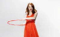 Emma Stone in a vibrant red dress joyfully hula hooping, showcasing her playful spirit and fashion sense.