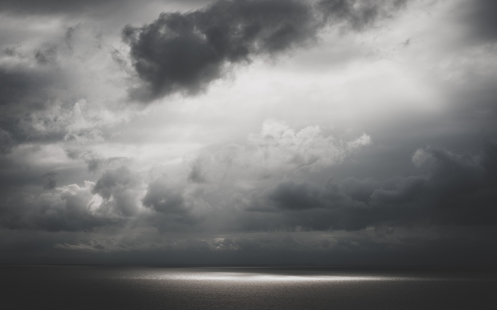 Des nuages sombres au-dessus de l'océan avec un bateau solitaire au loin (noir et blanc, nuage, blanc, noir, journée)