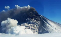 Stratovolcan en éruption contre un ciel clair avec des cendres volcaniques et des nuages cumulus.