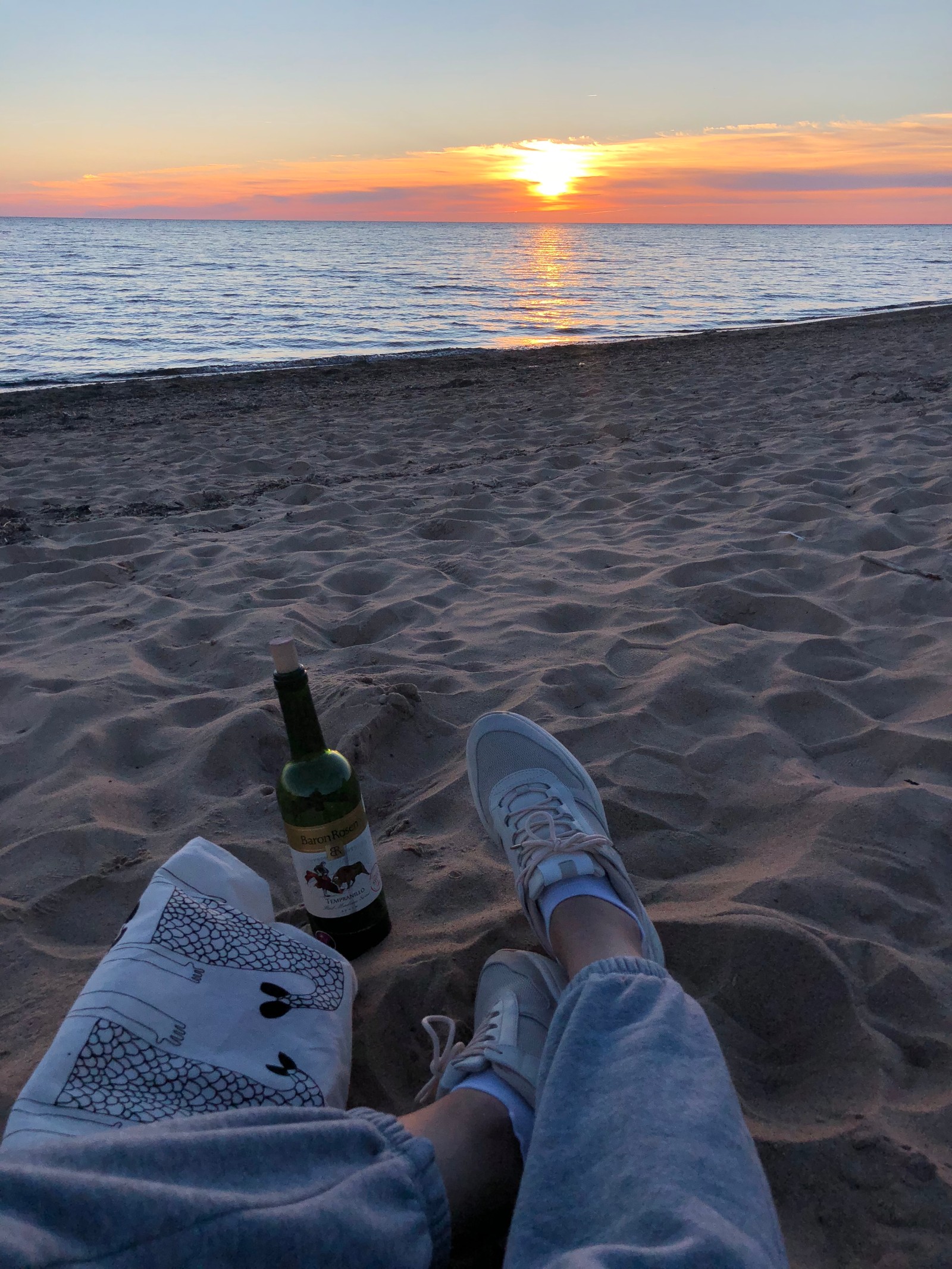 Someone is laying on the beach with a bottle of beer (sea, water, shoe, jeans, sunset)