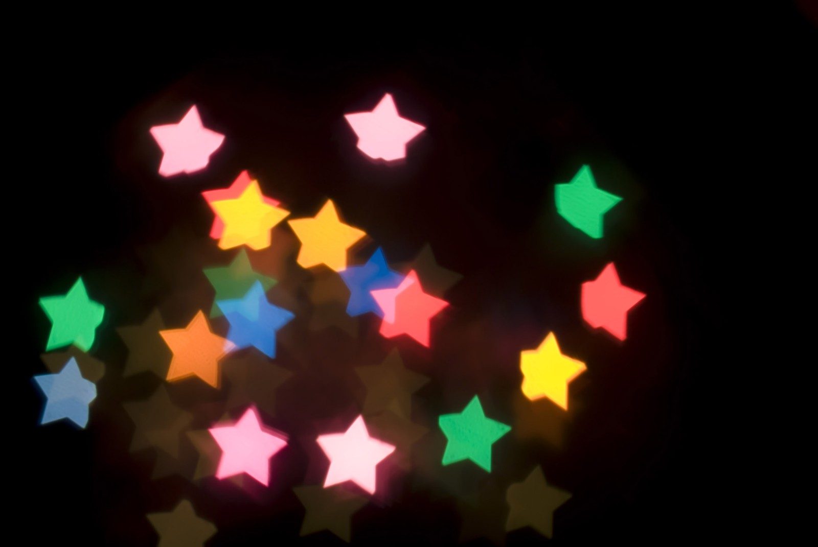 Estrelas coloridas dispostas em círculo em um fundo preto (bokeh, luz, iluminação, luzes de natal, natal)