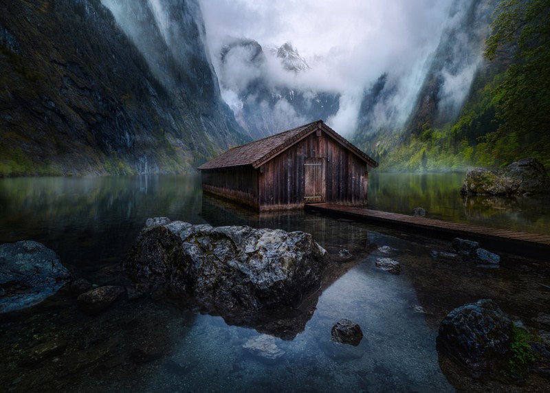 A close up of a boathouse on a lake with a mountain in the background (cabin, camping, lake)