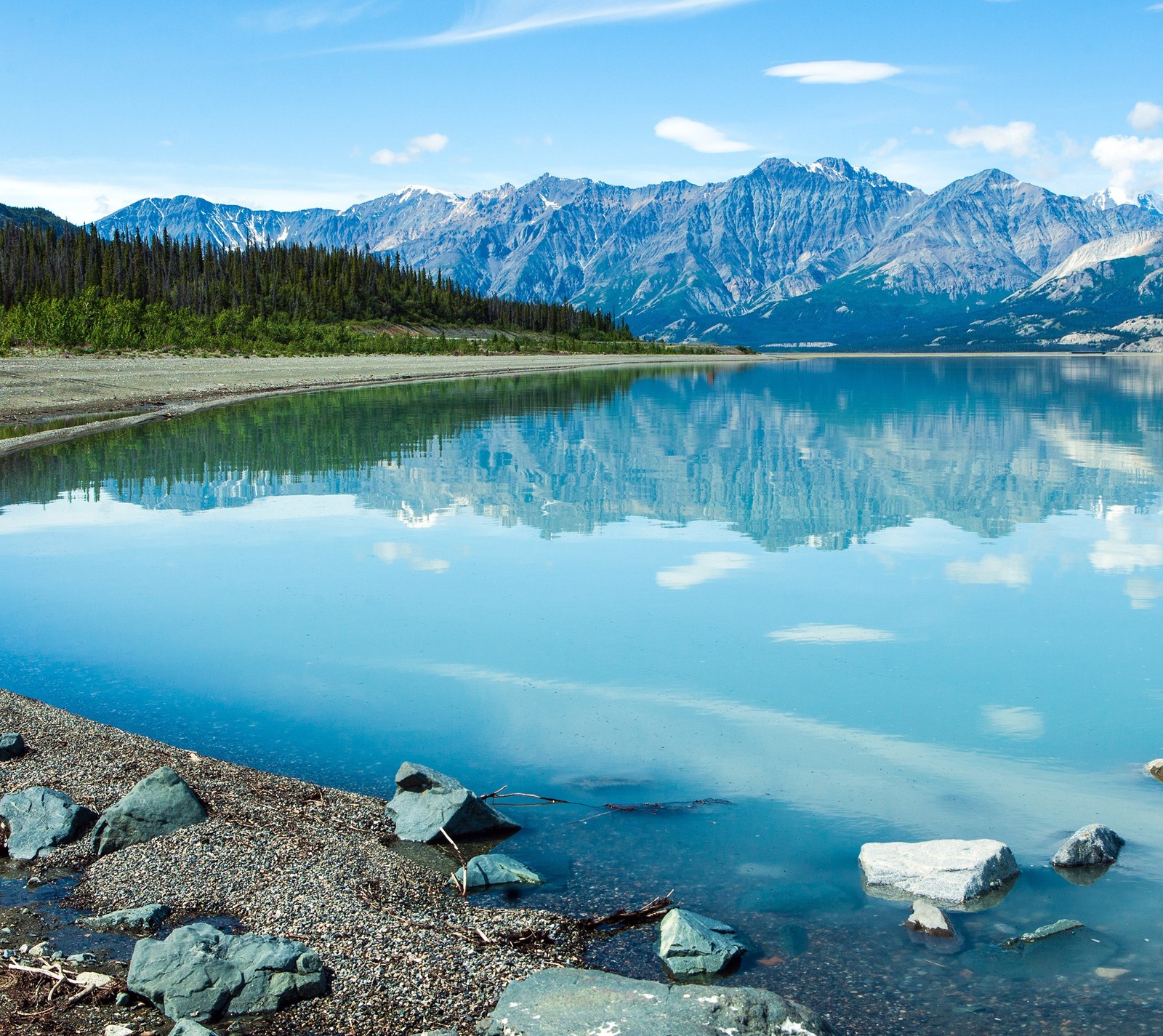 There is a lake with rocks and water in the middle of it (blue, canada, lake, mountains, trees)